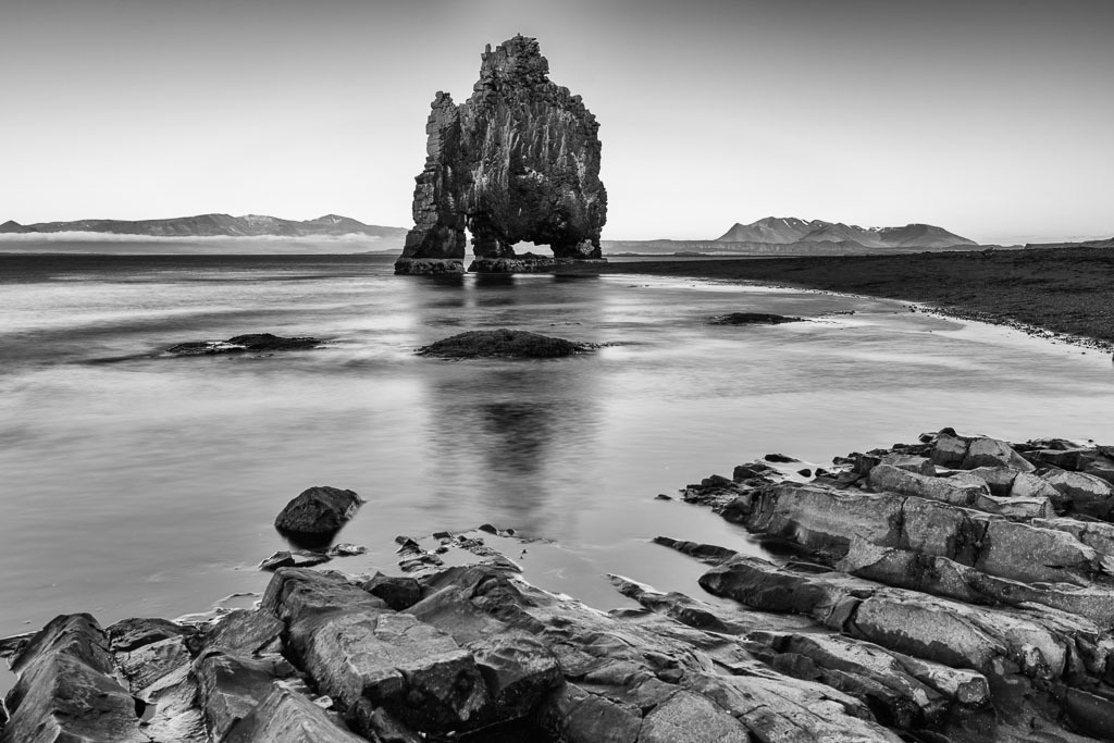 island-2019-164 | Der Hvítserkur (deutsch „weißer Kittel“, da durch Vogelexkremente weiß gefärbt) ist ein Basaltfelsen an der Ostküste der Halbinsel Vatnsnes im Nordwesten von Island. Der etwa 15 Meter hohe Felsen, der an zwei Stellen ausgehöhlt ist, liegt am Húnafjörður und ist Nistplatz verschiedener Vogelarten wie etwa der Dreizehenmöwe und des Eissturmvogels. - Realisiert mit Pictrs.com