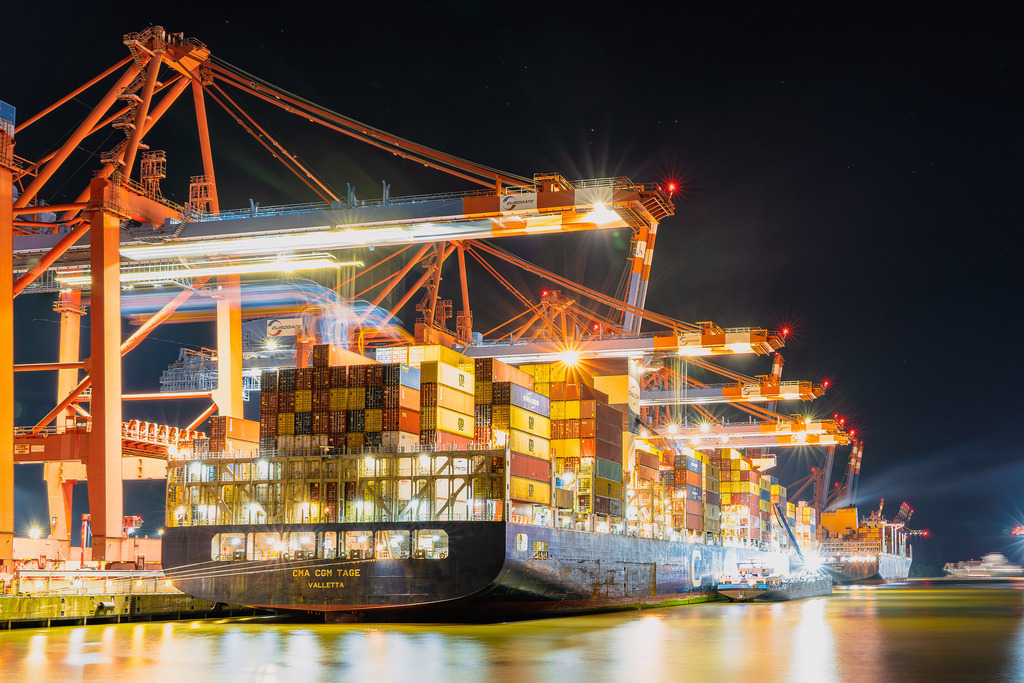 Nachtumschlag am Containerterminal | Ein Blick auf das Heck des Containerschiffs CMA CGM TAGE während des nächtlichen Umschlagbetriebs im Hamburger Hafen. Die Langzeitbelichtung dokumentiert die Bewegungsabläufe der Kräne und die Lichtreflexionen auf der Wasseroberfläche des Hafenbeckens. - Realisiert mit Pictrs.com