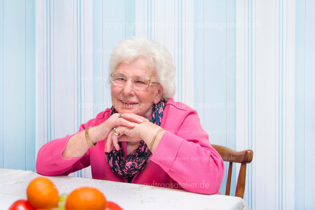 Seniorin sitzt am Tisch und denkt an was schönes vor blauer Streifentapete D | 80 jährige Seniorin sitzt entspannt an ihrem eigenen Tisch. Im Hintergrund bietet eine Tapete Copy Space. 