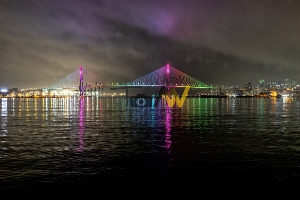 Die Busan Harbor Bridge in Busan bei Nacht------Regenbogen Farben | Das Bild zeigt die Busan Harbor Bridge (auch bekannt als Busan-Hang-Brücke) in Südkorea bei Nacht.Hier sind einige Details dazu:Die Brücke ist eine markante Schrägseilbrücke, die den Hafen von Busan überspannt.Sie ist bekannt für ihre farbenfrohe LED-Beleuchtung, die nachts in verschiedenen Farben leuchtet und sich im Wasser spiegelt. - Realisiert mit Pictrs.com
