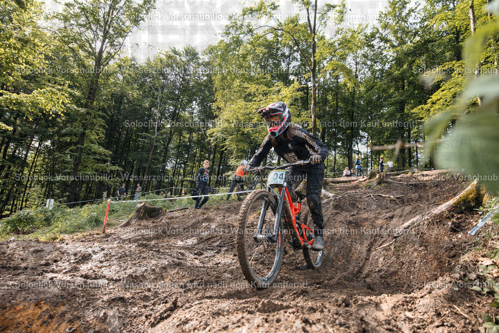 Mountainbiker im Sturmlauf | Ein Mountainbiker stürzt einen steilen, erdigen Hang hinunter, umgeben von dichtem Grün und Bäumen. Er trägt einen roten Mountainbike-Helm und eine Schutzkleidung und fährt mit hoher Geschwindigkeit. - Realisiert mit Pictrs.com