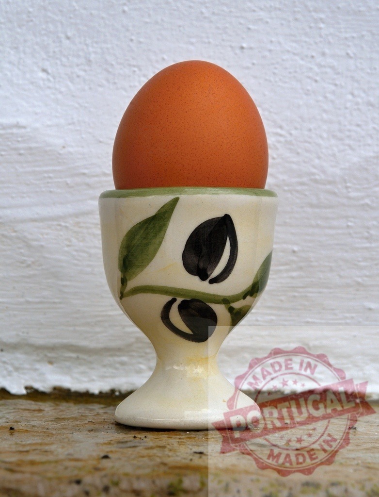 Brown egg resting in hand-painted ceramic egg cup | Brown egg sitting in an illustrative ceramic egg cup on a rustic surface - Realisiert mit Pictrs.com