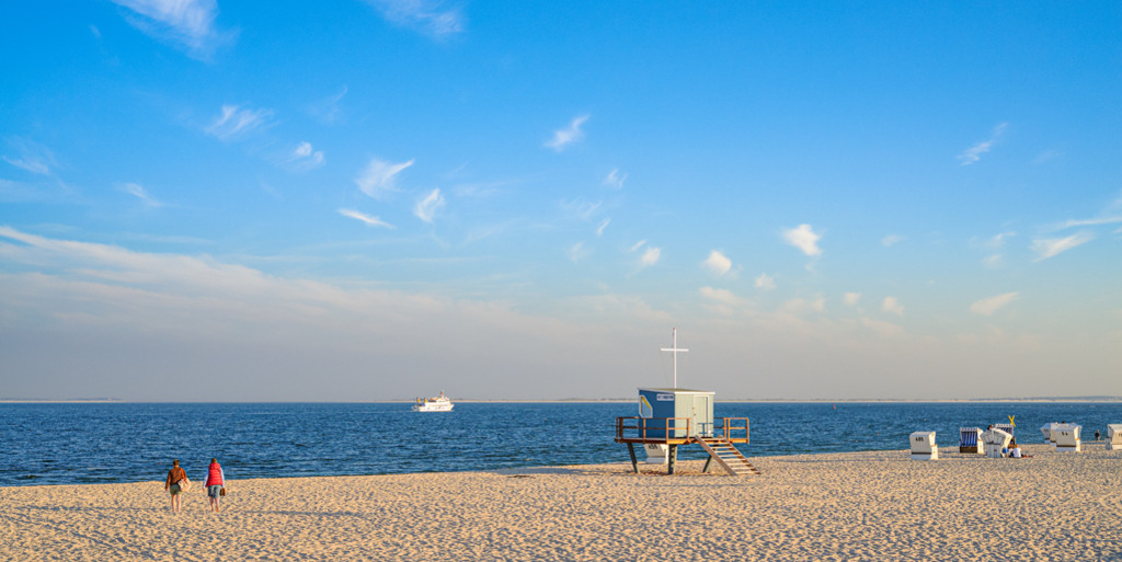 Strand in Hörnum | Abendlicht am Strand von Hörnum auf der Insel Sylt. Letzte Strandbesucher genießen den malerischen Tagesabschluss, ein letztes Schiff fährt draußen auf See von Insel zu Insel. — Auflösung des Originals: 6016 x 3008 px. - Realisiert mit Pictrs.com