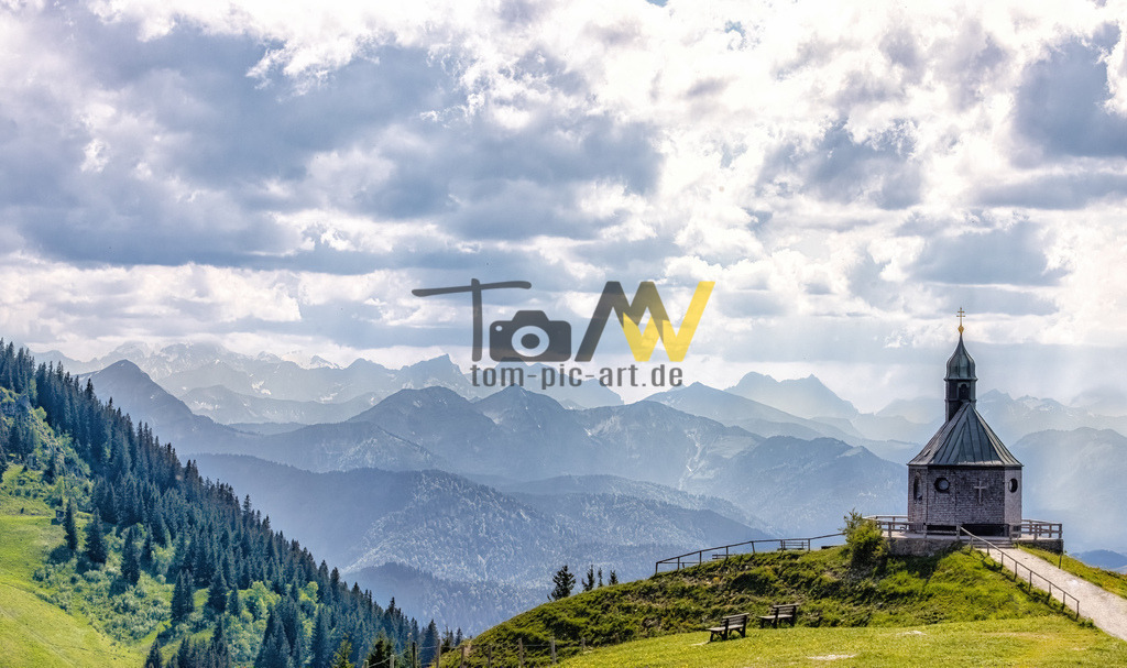 Kirche auf dem Wallberg mit Alpenpanorama--------Tegernsee | Die abgebildete Kapelle ist die Heilig-Kreuz-Kirche (auch Wallbergkapelle oder Wallbergkirchlein genannt) auf dem Wallberg in den bayerischen Alpen. Die Kapelle befindet sich in der Nähe der Bergstation der Wallbergbahn und bietet einen weiten Blick über den Tegernsee. Sie wurde 1909 fertiggestellt und gehört zum Erzbistum München. Während der Sommermonate (Juni bis September) finden sonntags Gottesdienste statt. Die Kapelle ist ein beliebtes Ziel für Wanderer und Touristen.  - Realisiert mit Pictrs.com