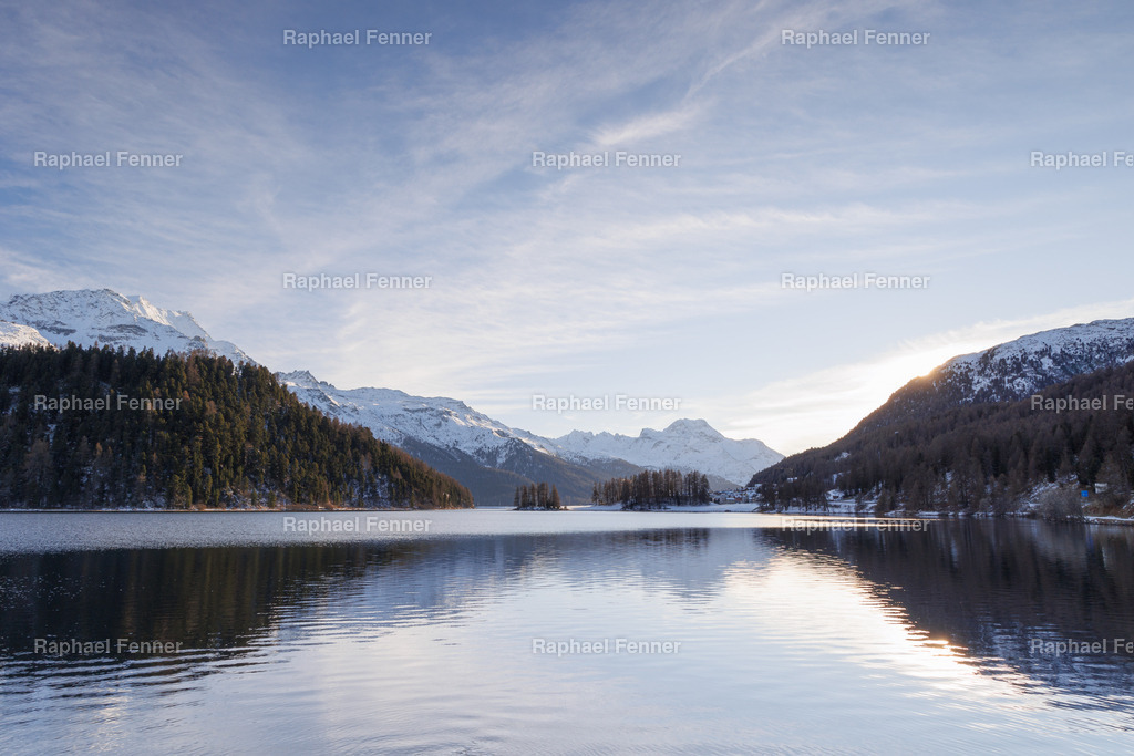Spätnachmittag am Lej da Champfèr | Ein weiter Blick über den Lej da Champfèr an einem klaren Winternachmittag. Die Sonne steht bereits tief, das Licht ist weich und warm, während sich Berge und Himmel sanft im stillen Wasser spiegeln. Diese Aufnahme bringt die besondere Stimmung später Wintertage ins Zuhause – ruhig, weit und voller Licht.
