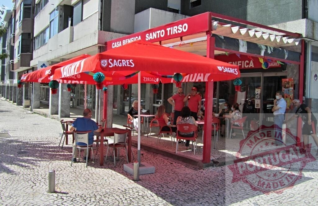 People enjoying outdoor cafe seating at Casa Benfica | Patrons relaxing under red Sagres beer umbrellas at an outdoor Portuguese cafe - Realisiert mit Pictrs.com