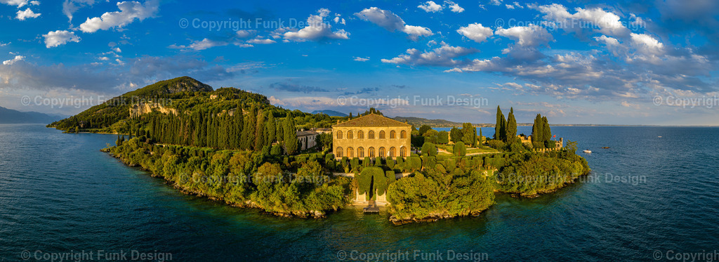 Villa San Vigilio im Abendlicht – Gardasee, Venetien, Italien | Die Villa San Vigilio liegt wie ein kleines Paradies am Gardasee: Zypressen, gepflegte Gärten und warmes Abendlicht treffen auf das ruhige, tiefblaue Wasser. Aus der Luft wirkt die Halbinsel besonders edel und zeitlos und bringt mediterrane Eleganz als Panorama-Wandbild in jeden Raum.