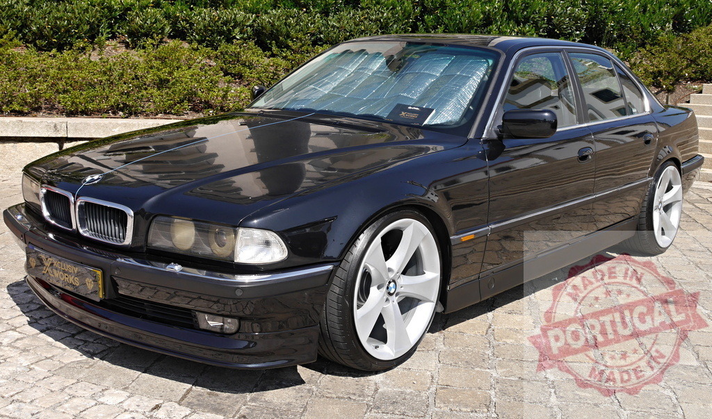 BMW 7 Series E38 black luxury sedan parked outdoors | Black BMW 7 Series E38 sedan with custom wheels and a sunshade parked on cobblestones - Realized with Pictrs.com