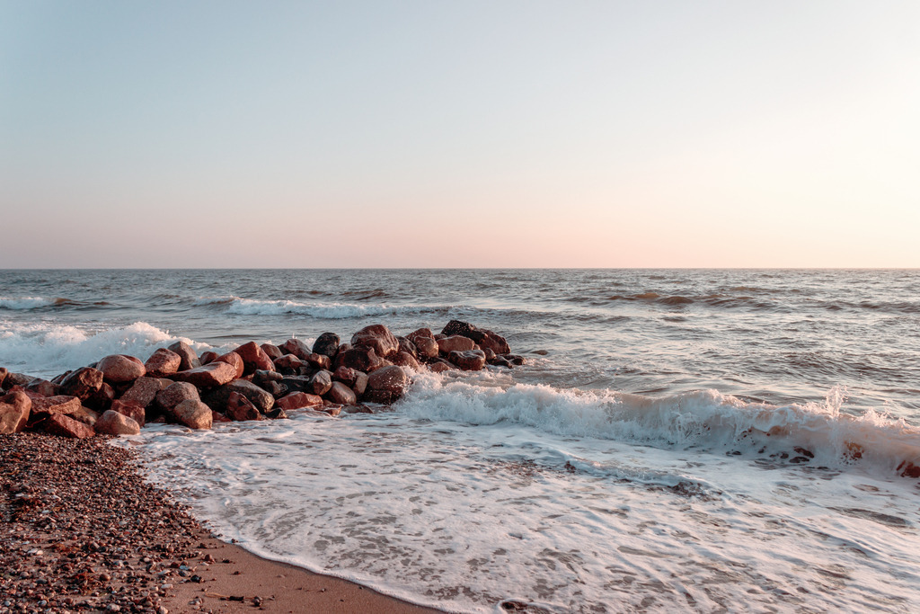 Wandbild: Wellen am Sandstrand im Morgenrot | Dieses Wandbild im Querformat zeigt eine wunderschöne Morgenstimmung am Meer. Zu sehen sind Wellen im Morgenrot, die am Sandstrand auslaufen. Vom Strand ragt eine Steinmole ins Meer. Der Himmel leuchtet in dezenten Farben von einem hellen blau bis hin zu einem leichten rotorange. Holen Sie sich diese schöne maritime Morgenstimmung auf Leinwand, Aluminium-Platte oder als Glasbild. Ideal fürs Wohnzimmer, Schlafzimmer, Küche, den Arbeitsplatz oder die Ferienwohnung. Die Wandbilder werden individuell für Sie in vielen Abmessungen produziert. - Realisiert mit Pictrs.com