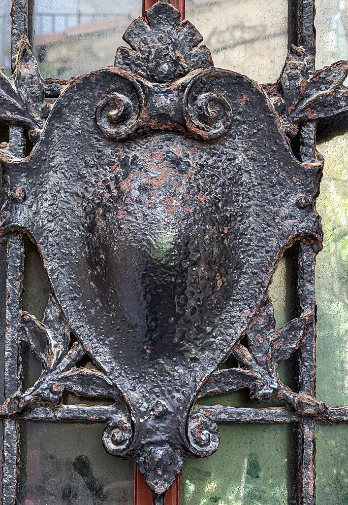 Iron Heritage – Historisches Wappen-Detail | Kunsthandwerk vergangener Zeiten: Diese detailreiche Fine-Art-Fotografie fängt ein prachtvolles, geschmiedetes Türornament mit einem zentralen Wappenschild ein. Die faszinierende Patina, die feinen Rost-Nuancen und das meisterhaft verarbeitete Eisen zeugen von historischer Eleganz. Ein ausdrucksstarkes Kunstwerk, das durch seine tiefen Kontraste besticht und klassischen Galerie-Charakter in moderne Wohnzimmer, Lofts oder stilvolle Arbeitszimmer bringt.▶ Material-Empfehlung: Als großformatiger Druck unter edlem, glänzendem Acrylglas oder auf mattem Alu-Dibond kommen die metallischen Reflexe und das tiefe Schwarz dieses historischen Kunstwerks besonders kraftvoll, edel und tiefenwirksam zur Geltung.Wähle jetzt deine Wunschgröße aus und bringe echte Handwerks-Ästhetik an deine Wand![Archiv-Nr. #9855] - Realisiert mit Pictrs.com