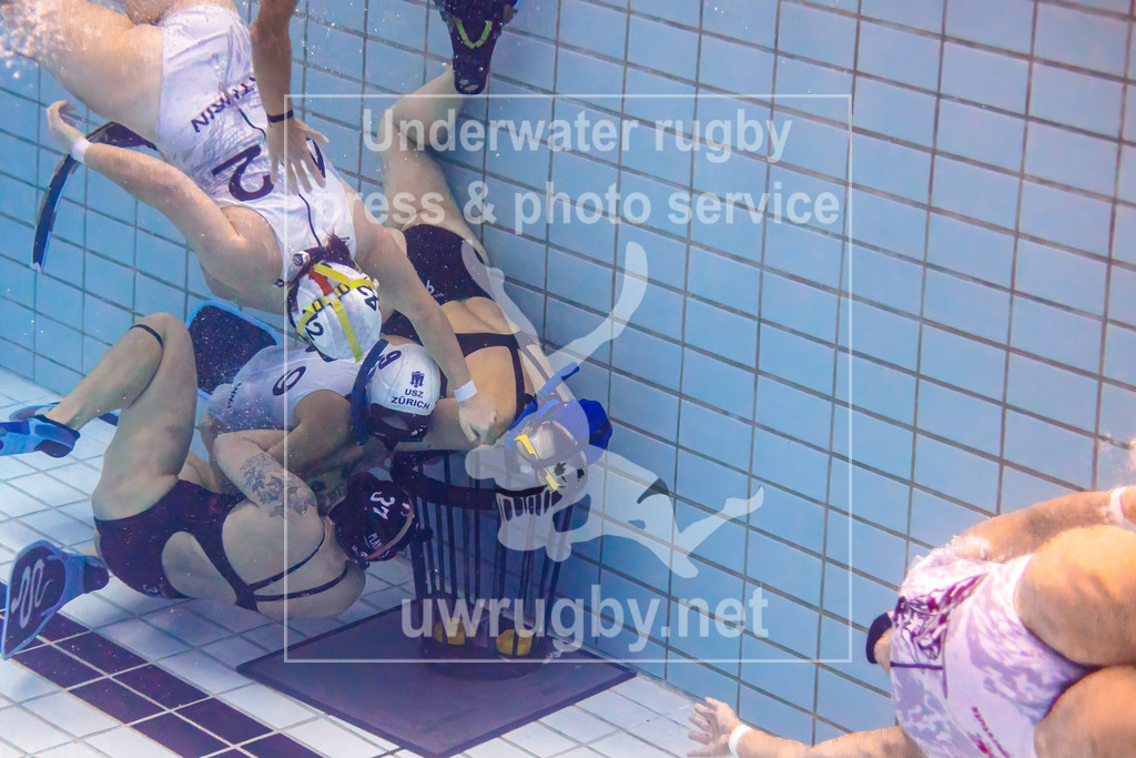 24. - 26.11.2023: Unterwasser-Rugby Champions Cup 2023  | Damen-Spiel: UWRC Wien (Österreich) in blau gegen Helvetia (Schweiz) in weiß. Anna Stampfli (weiß #9) kämpft mit der österreichischen Verteidigerin Denise Schmutz (blau #37) direkt vor dem leeren Korb um den Ball. Ulrike Janovsky (blau #9) versucht provisorisch den Korb zu beschützen. - Realisiert mit Pictrs.com