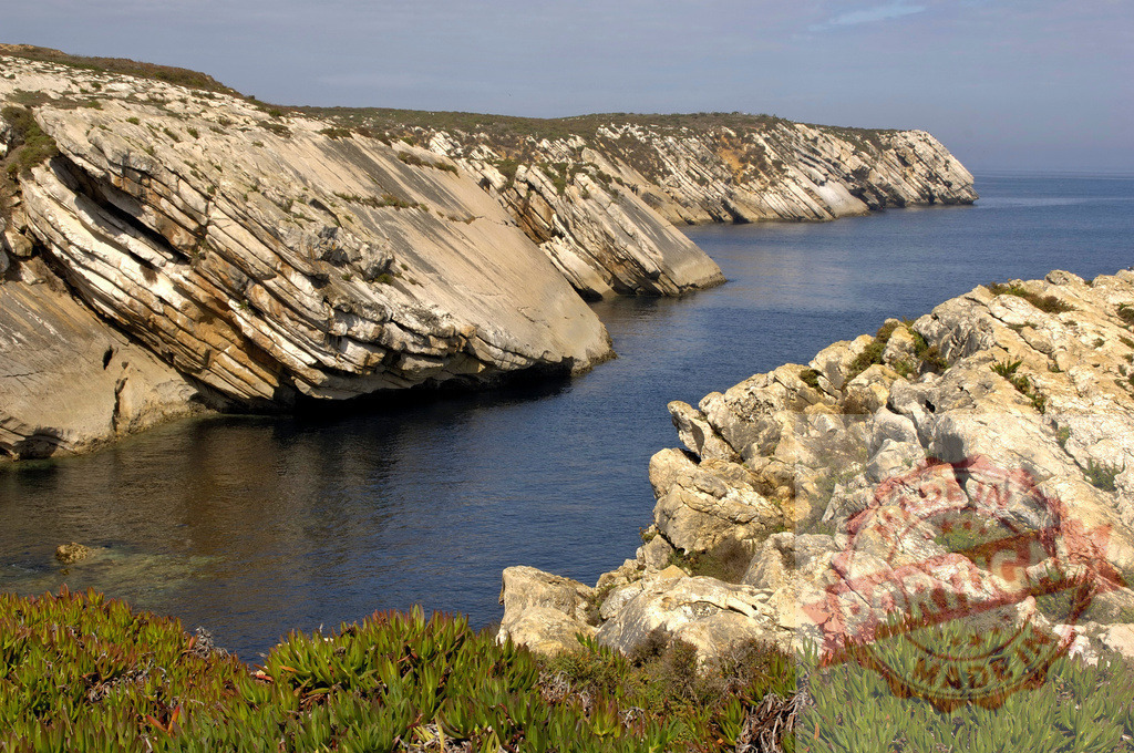 Portuguese coastline showing prominent rock strata and ocean landscape | Steep coastal cliffs reveal distinct geological layers meeting the calm Atlantic Ocean - Realized with Pictrs.com