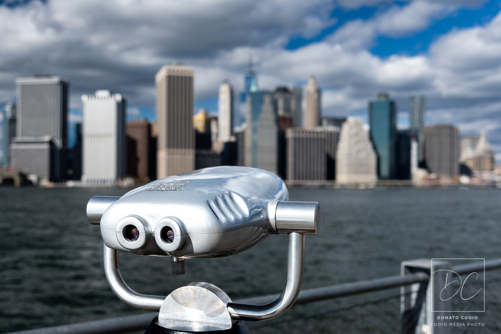 Looking into 2026 – Modern Silence Fine Art Print | Dieses Fine-Art-Foto zeigt ein modernes Fernglas mit Blick auf die verschwommene Skyline von Manhattan.Die reduzierte Komposition und die ruhige Farbigkeit erzeugen ein Gefühl von Weite, Zukunft und Richtung.Ein Bild über Perspektive, Möglichkeiten und den offenen Blick nach vorn.Ein modernes Statement-Piece für stilvolle Wohnräume, Büros und minimalistische Interiors. - Realisiert mit Pictrs.com