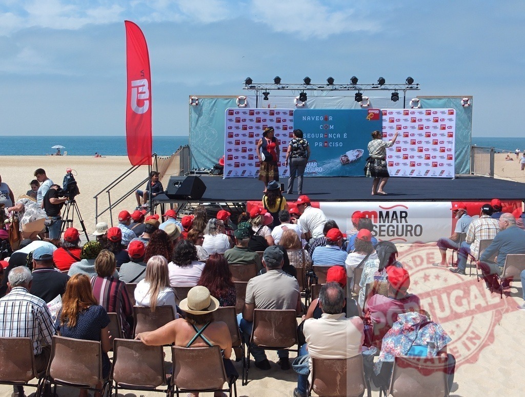 Audience wearing red caps watching actors performing on stage at beach event | Audience wearing red caps watching actors performing on stage at beach event promoting safe sea navigation - Realized with Pictrs.com