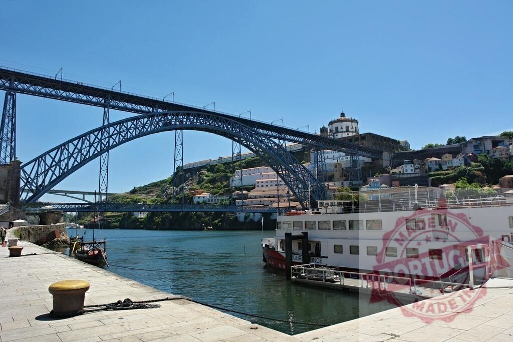 Dom Luis I Bridge spanning Douro River in Porto | Steel arch bridge crossing the Douro River with a cruise boat docked on a sunny day - Realized with Pictrs.com