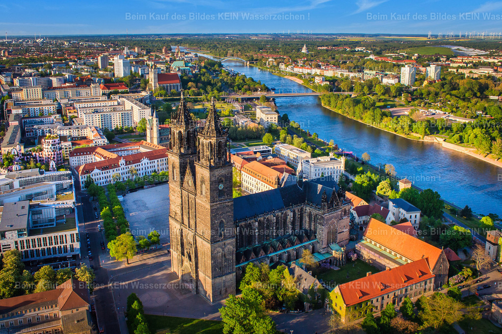 Luftbild_Magdeburg_Dom_Skyline_2016_Elbe-6712 | Dieses Luftbild zeigt den Magdeburger Dom an einem sonnigen Tag aus einer eindrucksvollen Perspektive über der Elbe. Die Aufnahme entstand bereits im Jahr 2016 und wurde nun erneut digital bearbeitet, um die Details, Farben und die besondere Atmosphäre des Motivs noch stärker hervorzuheben.Die Elbe führt den Blick des Betrachters direkt auf das Hauptmotiv, den Magdeburger Dom. Als älteste gotische Kathedrale Deutschlands prägt das Bauwerk seit Jahrhunderten die Silhouette der Landeshauptstadt Sachsen-Anhalts. Aus der Vogelperspektive wird die besondere Lage des Doms am Elbufer sowie seine Einbindung in das historische Stadtzentrum besonders deutlich sichtbar.Das sonnige Wetter sorgt für klare Konturen und eine hohe Detailtiefe. Die neu überarbeitete Bildbearbeitung verleiht der Aufnahme zusätzliche Brillanz und betont die harmonische Verbindung zwischen Flusslandschaft, historischer Architektur und urbanem Raum.Dieses Luftbild dokumentiert nicht nur eines der bedeutendsten Wahrzeichen Magdeburgs, sondern zeigt auch die zeitlose Schönheit der Stadt aus einer Perspektive, die nur aus der Luft erlebbar ist. - Realisiert mit Pictrs.com