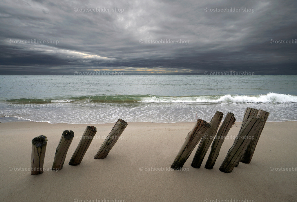 Blick auf dunkle Wolken über der Lübecker Bucht | Windschiefe Pfähle eines alten Wellenbrechers erwarten eine heraufziehende Regenfront über der Lübecker Bucht.
