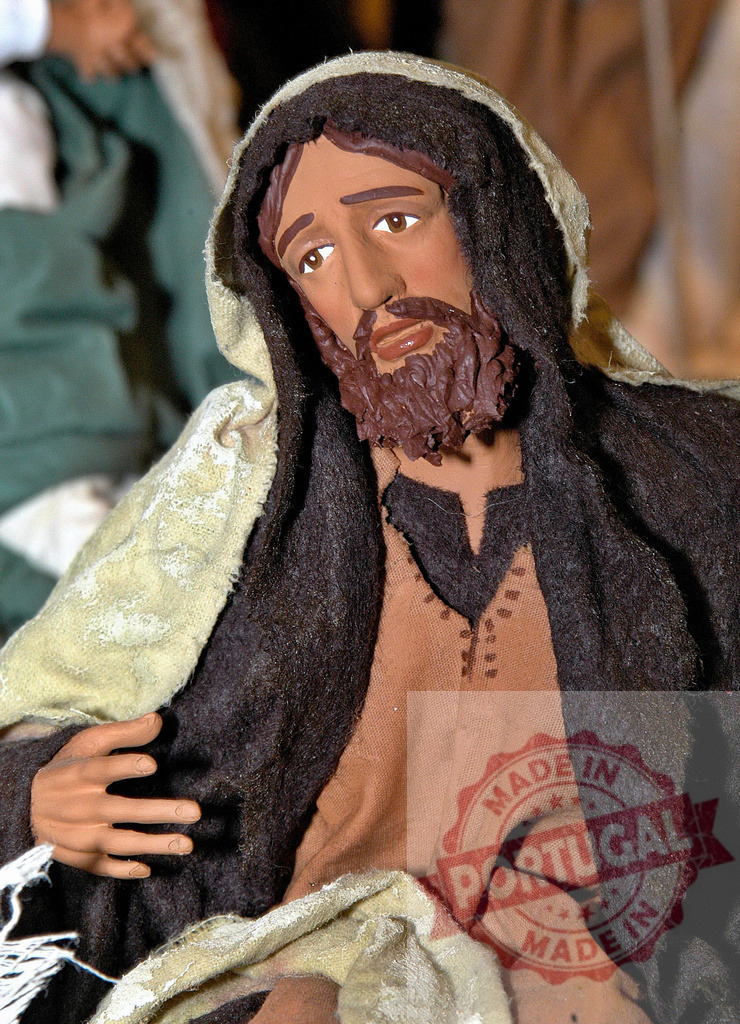 Saint Joseph figurine wearing dark clothes and cloak is sitting in the Nativity scene | Saint Joseph statue is part of a Christmas Nativity scene, representing the birth of Jesus - Realized with Pictrs.com