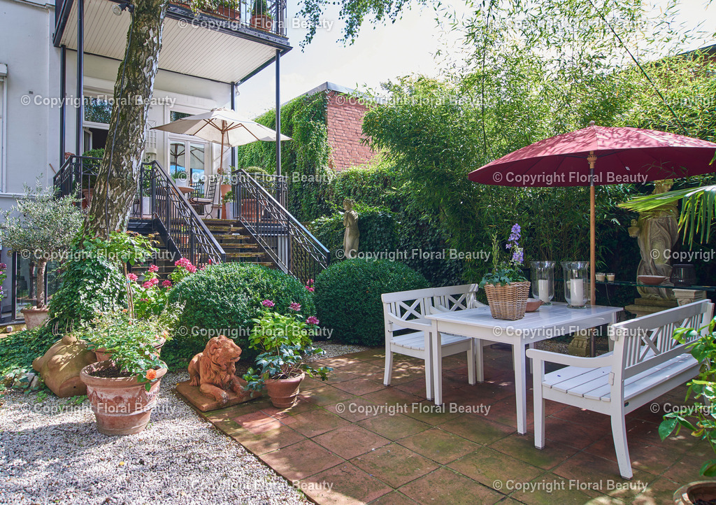 Mediterraner Stadtgarten | Städtischer Garten mit Treppenaufgang zum Balkon. Weiße Gartenmöbel und Tonstatuen. - Realisiert mit Pictrs.com