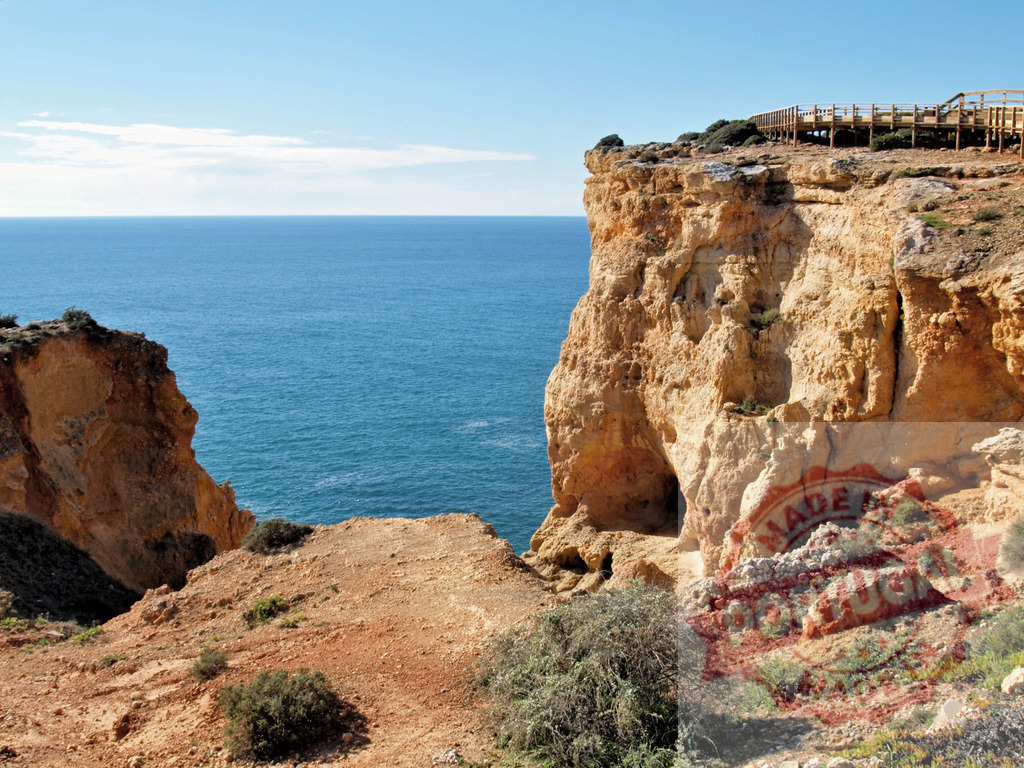 Algarve cliff with ocean and boardwalk on a sunny day | Algarve coast featuring rugged sandstone cliffs, grottos, and an ocean view under a clear sky - Realized with Pictrs.com