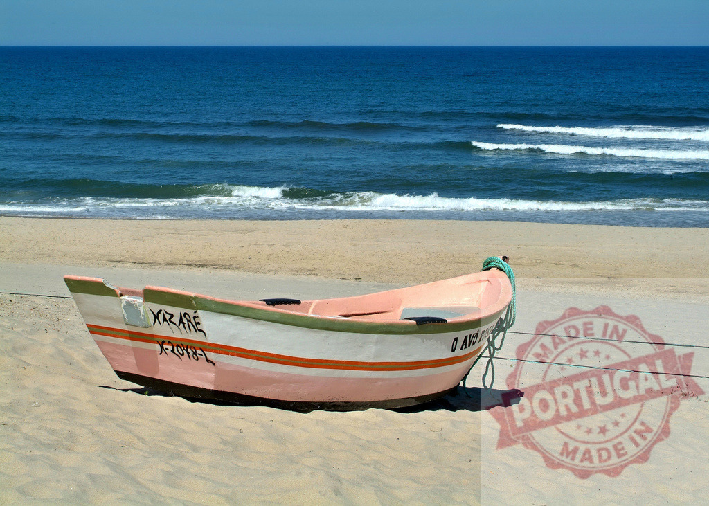Fishing boat resting on Nazaré beach sand | Fishing boat resting on a sandy beach with ocean waves breaking in the background - Realized with Pictrs.com