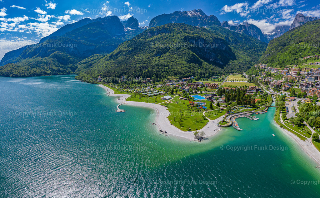 Drohnenpanorama über dem Molvenosee – Molveno, Trentino, Italien | Diese Drohnenaufnahme zeigt den Molvenosee in seiner ganzen Pracht: türkisfarbenes Wasser, das geschwungene Ufer mit Strand und Hafen sowie die mächtige Bergkulisse rund um Molveno. Ein starkes Sommermotiv aus dem Trentino, das als Panorama-Wandbild sofort Urlaubsgefühl und Weite in den Raum bringt.