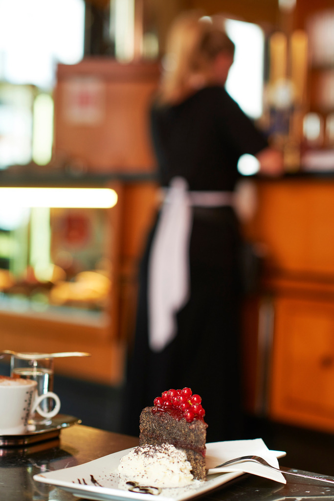Cafe Goldegg | Wien, Austria - August 29, 2017: Cafe Goldegg, eine garnierte Mohntorte mit Melange steht auf dem Tisch, im Hintergrund eine Kellnerin. - Realisiert mit Pictrs.com