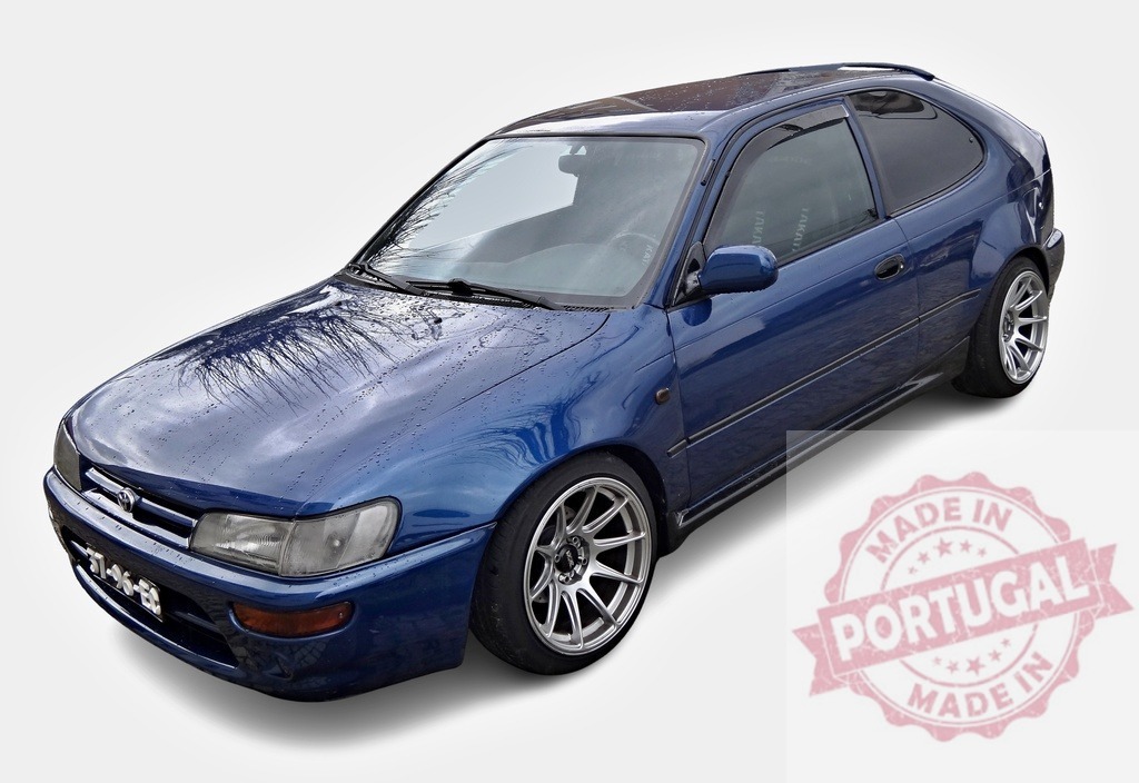 Tuned Toyota Corolla E10 lifting showing alloy rims and wet bodywork | Modified Japanese compact car parked after a car wash, reflecting trees in the wet hood - Realisiert mit Pictrs.com