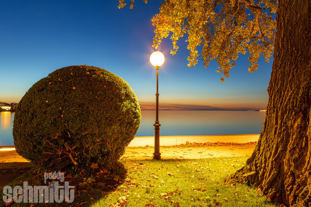 Seeufer bei Bregenz am Bodensee bei Nacht | Am nächtlichen Bodenseeufer bei Bregenz setzt eine leuchtende Laterne einen warmen, stimmungsvollen Akzent in der Dunkelheit. Das ruhige Wasser und die nächtliche Atmosphäre verleihen der Aufnahme eine besondere Ruhe und einen Hauch von Romantik. - Realisiert mit Pictrs.com