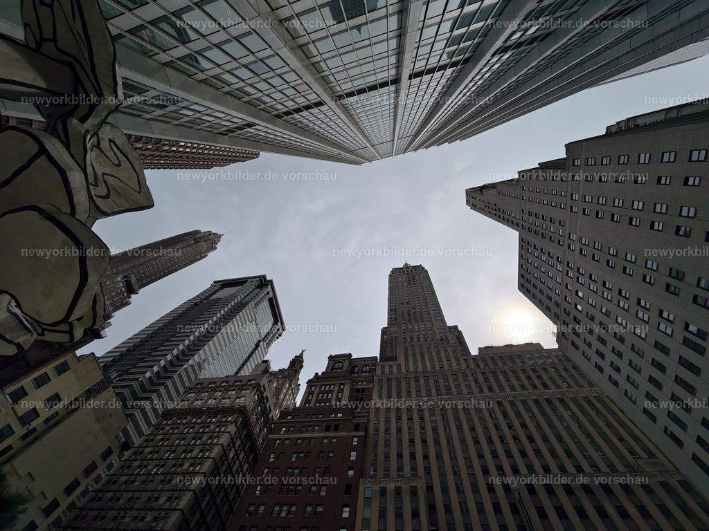 Umgeben von Wolkenkratzern nahe der Wall Street – Ein Blick voller Kontraste und Macht | Die Straßen nahe der Wall Street und in unmittelbarer Nachbarschaft wirken wie tiefe Schluchten, eingerahmt von Wolkenkratzern, die sich kühn in den Himmel strecken. Glas, Stahl und Stein verschmelzen zu einer Kulisse, die Macht und Geschichte ausstrahlt. Zwischen den Schatten der Hochhäuser fließt das Leben der Stadt – Menschen eilen vorbei, Stimmen hallen, und über allem liegt das Gefühl von Dynamik und Ehrgeiz. Die Architektur erzählt von einer Welt, in der Entscheidungen Milliarden bewegen, während die Sonne nur in schmalen Streifen den Asphalt erreicht. Dieser Blickwinkel ist mehr als ein Foto – er ist ein Sinnbild für die Energie und den Rhythmus einer Stadt, die niemals stillsteht