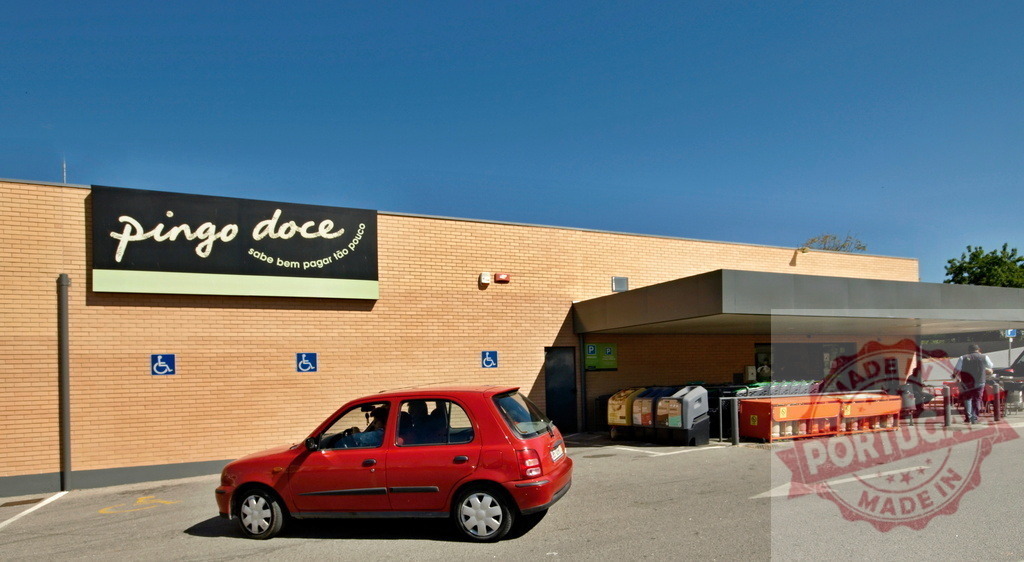 Pingo Doce supermarket exterior and parking lot on a sunny day | Pingo Doce supermarket exterior showing its sign, building, parking lot, and customer cars - Realisiert mit Pictrs.com