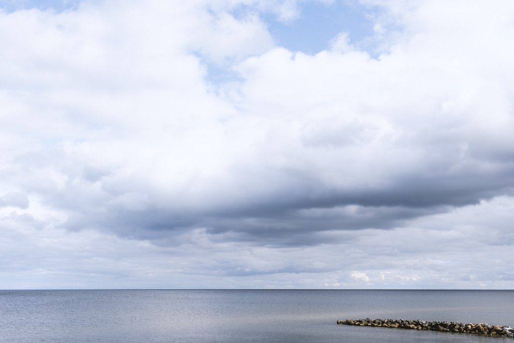 Akustikbild: Steinmole an der stillen See – Weite Küstenklarheit | Dieses Wandbild zeigt eine Steinmole, die in die stille See ragt, unter einem weiten, wolkigen Himmel. Die sanfte Wasserfläche und die ruhige Horizontlinie vermitteln Klarheit, Weite und eine natürliche, norddeutsche Küstenatmosphäre. Als Akustikbild verbessert es die Raumakustik, reduziert Nachhall und sorgt für eine angenehm gedämpfte Klangkulisse.