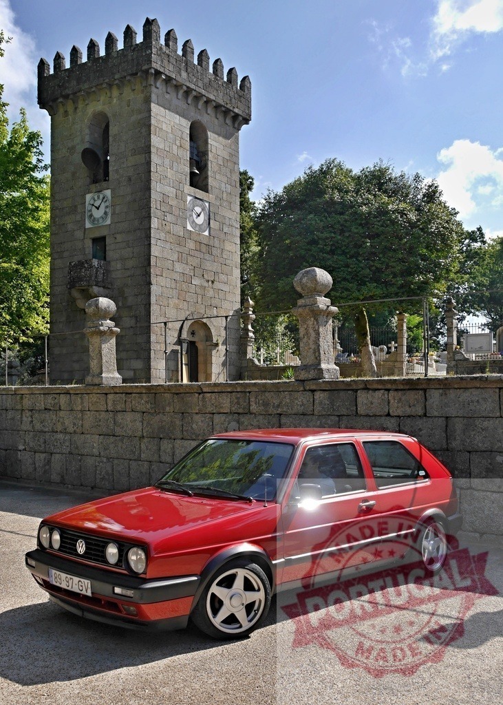 Red Volkswagen Golf Mk2 parked near a bell tower | Red Volkswagen Golf Mk2 standing proudly beside a historic stone bell tower, representing classic style - Realisiert mit Pictrs.com