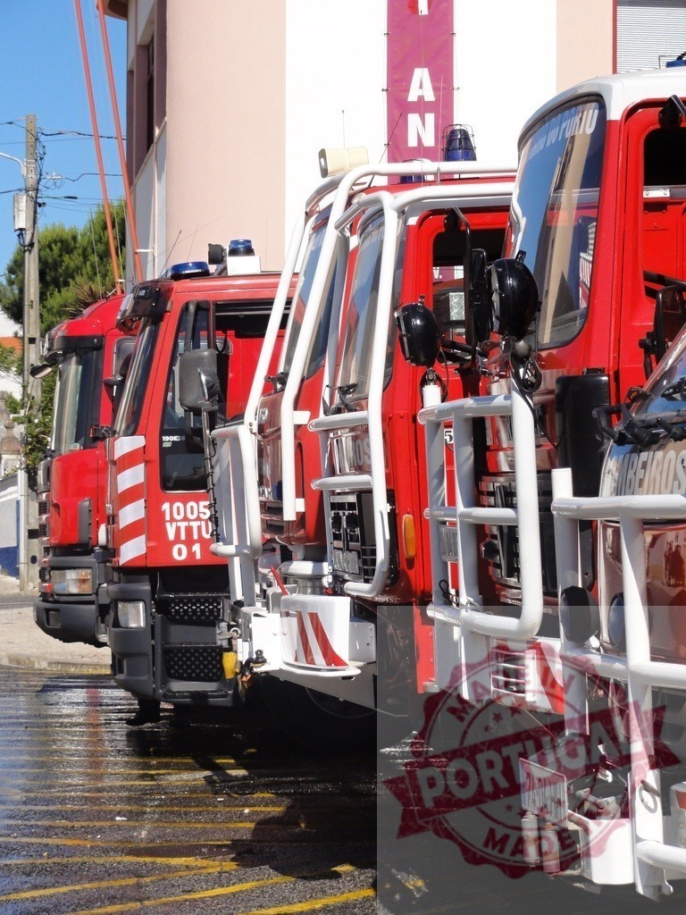 Portuguese firefighters vehicles parked and ready for service | Row of red fire trucks parked outside a station, reflecting on wet asphalt - Realized with Pictrs.com