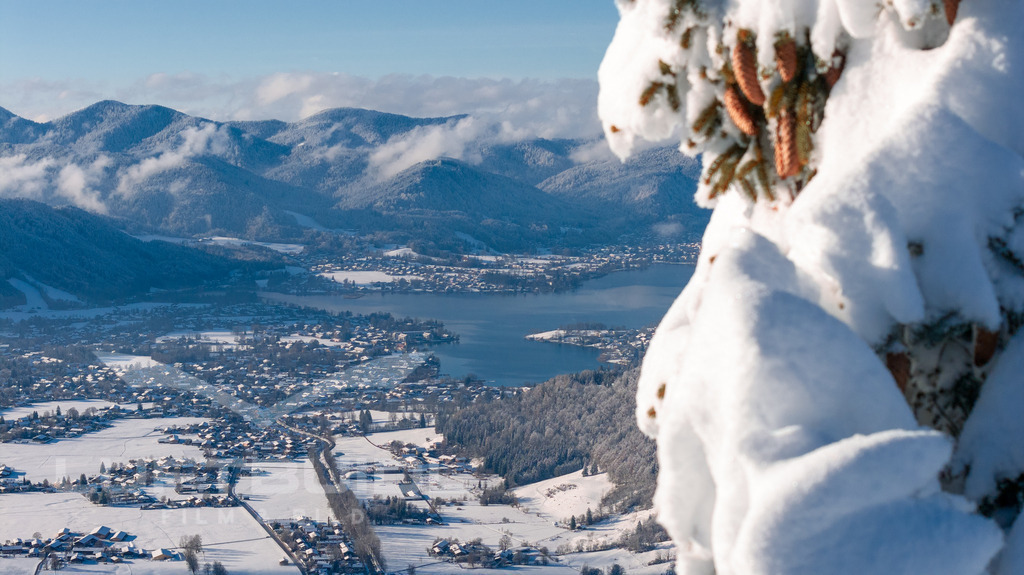 Blick von der Rinnerspitz gen Rottach-Egern (Fokus Tal); W45 | Ein winterlicher Blick von der Rinnerspitz hinunter ins Tegernseer Tal: Verschneite Hänge rahmen den tiefblauen Tegernsee ein, während sich Rottach-Egern ruhig und fast märchenhaft unter einer weißen Decke ausbreitet. Die klare Luft und die weite Sicht machen diesen Moment zu etwas ganz Besonderem: Ein stiller Augenblick hoch über dem Tal, der die Schönheit des Winters in den bayerischen Alpen eindrucksvoll zeigt. - Realisiert mit Pictrs.com