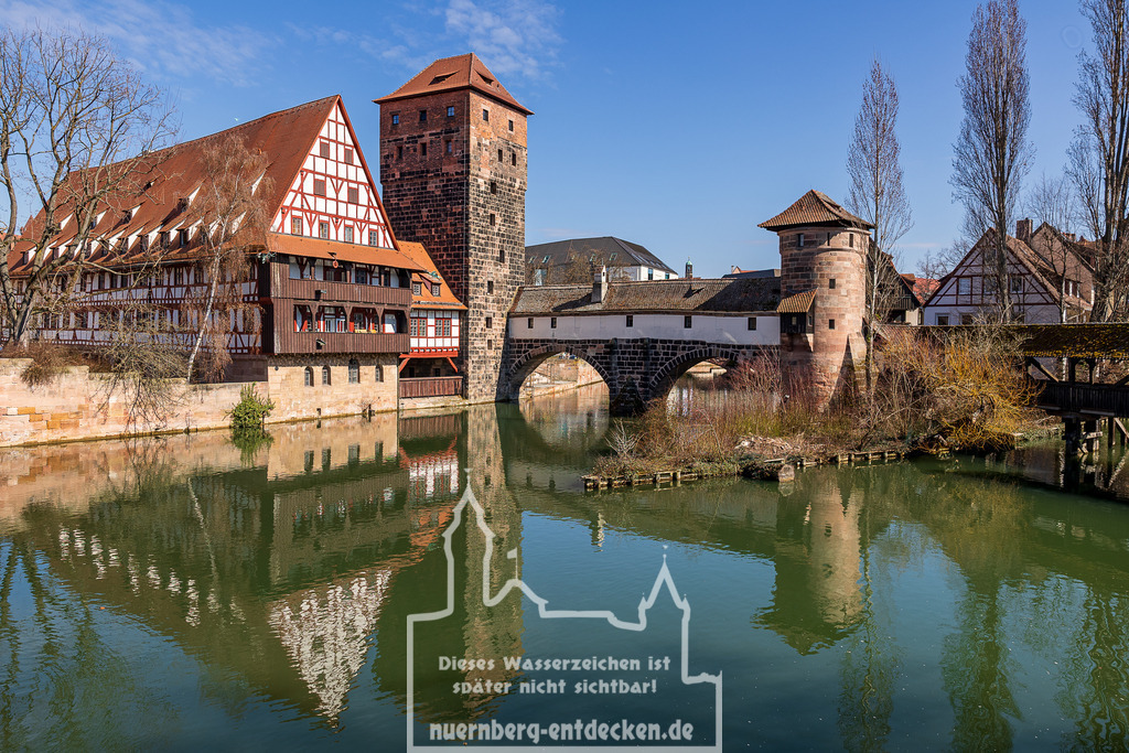 Nürnberger Stadtblick, 20.03.2025 | Der Weinstadel, die Henkersteg-Brücke und der Wasserturm spiegeln sich an einem sonnigen Frühlingsanfang in der Pegnitz. Die Fachwerkarchitektur und die historischen Türme gehören zu den bekanntesten Wahrzeichen Nürnbergs. Erste grüne Blätter und Blüten kündigen den Frühling an. - Realisiert mit Pictrs.com