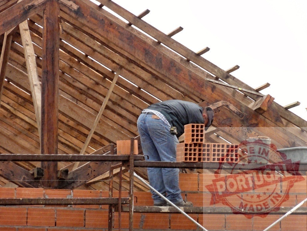 Construction worker building house roof scaffolding bricks | Construction worker laying bricks for a house wall on scaffolding under a wooden roof frame - Realized with Pictrs.com