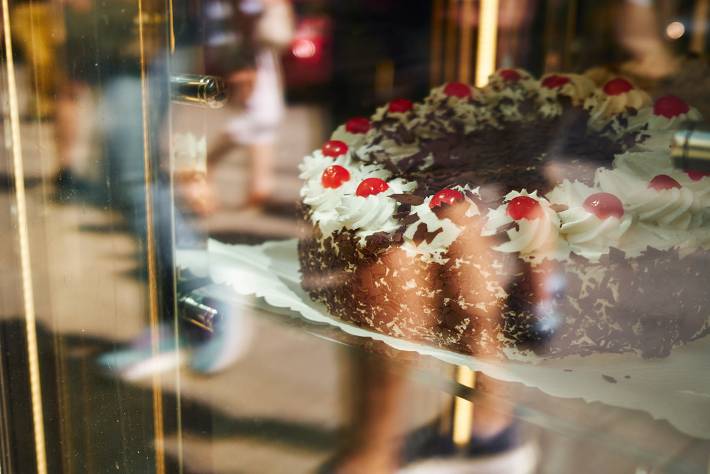 Schwarzwälder Kirschtorte im Schaufenster | Wien, Austria - June 12, 2025: Schwarzwälder Kirschtorte im Schaufenster mit Spiegelung von Menschen. - Realisiert mit Pictrs.com