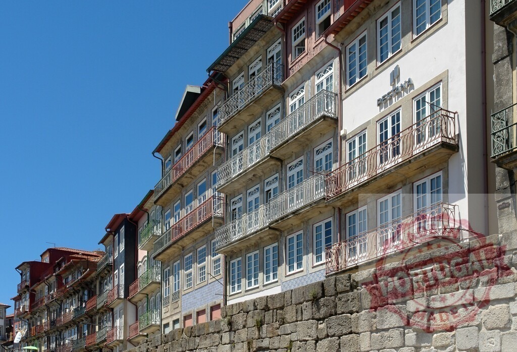 Porto, Portugal cityscape featuring Ribeira architecture and old town buildings. Porto - Portugal | Historic Ribeira buildings with traditional balconies and windows lining a stone wall, blue sky - Realisiert mit Pictrs.com