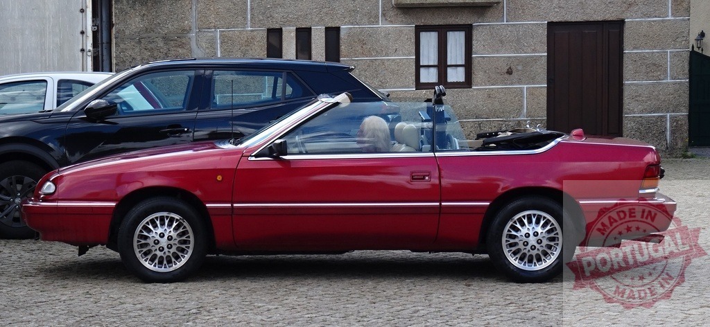 Red convertible car parked on a cobblestone street | Red classic convertible car parked on a European street with a building in the background - Realized with Pictrs.com