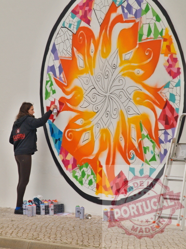 Woman artist creating street art mural with spray paint | Woman artist painting a colorful mandala street art mural on a white wall - Realisiert mit Pictrs.com