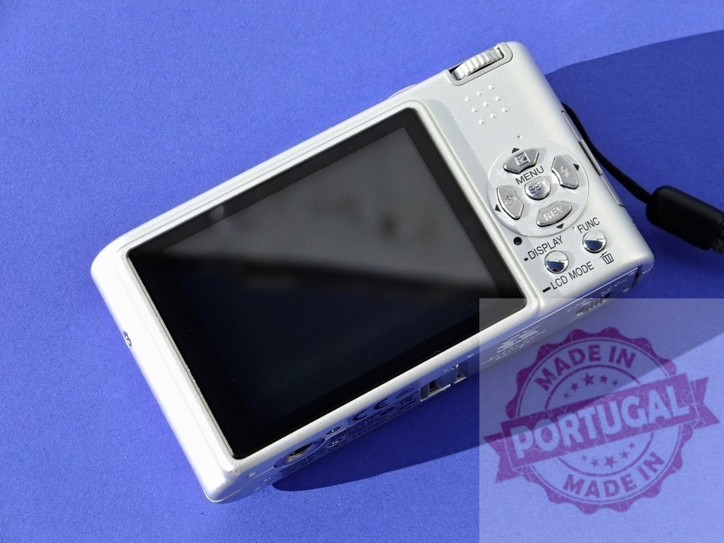Silver compact digital camera with LCD screen and control buttons | Digital camera lying on a blue background, showing its screen and controls - Realized with Pictrs.com