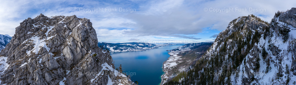 Winterpanorama über dem Attersee – Oberösterreich, Österreich | Ein dramatisches Winterpanorama öffnet den Blick über den Attersee: schroffe Felsen im Vordergrund, verschneite Hänge und ein tiefblauer See, der sich weit ins Tal zieht. Die Szene wirkt klar, kraftvoll und zugleich still und ist ideal als großes Panorama-Wandbild.