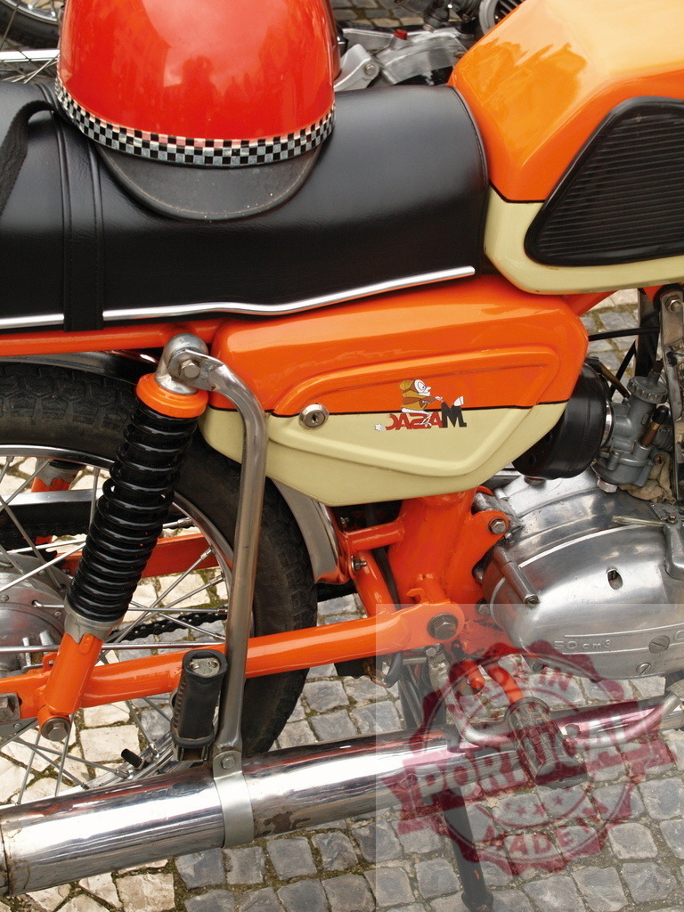 Orange jazam motorcycle with helmet parked on cobblestone street | Vintage orange jazam motorcycle parked on a cobblestone street with an orange helmet resting on the seat - Realisiert mit Pictrs.com