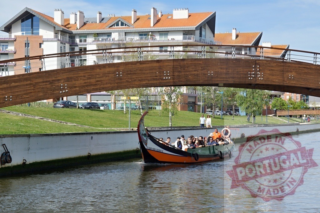 Aveiro canal with moliceiro boat under modern wooden bridge. Aveiro - Portugal | Moliceiro boat cruising a canal in Aveiro, Portugal, with tourists enjoying the tour - Realized with Pictrs.com