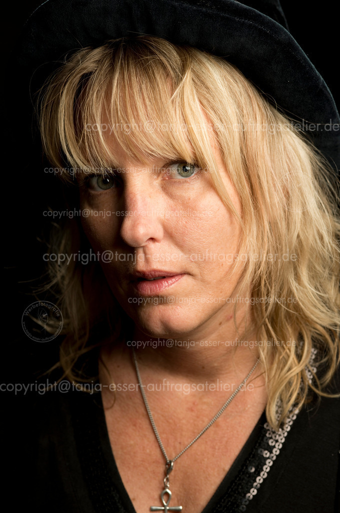 Blonde Frau mit schwarzem Hut D | Porträt einer blonden Frau mit schwarzem Hut. Sie schaut fragend in die Kamera. Sie wirkt verletzlich. Schwarzer Hintergrund. 