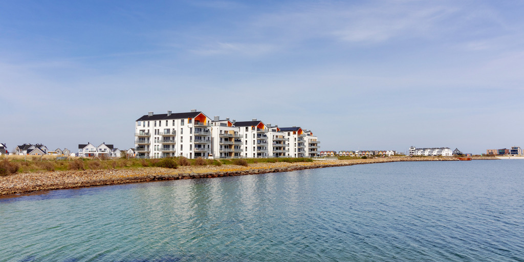 Panorama: Ferienwohnungen am Meer in Olpenitz | Dieses Panorama Wandbild zeigt Ferienwohnungen direkt am Meer in Olpenitz. Die Ferienwohnungen spiegeln sich auf dem Wasser. Am blauen Himmel befinden sich Schleierwolken.  - Realisiert mit Pictrs.com