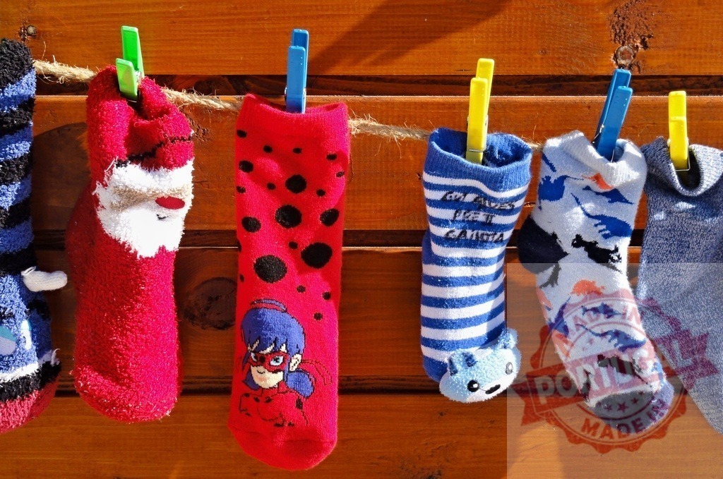 Colorful children's socks hanging and drying on a clothesline | Various colorful children's socks with different patterns are hanging on a clothesline to dry against a wooden wall - Realized with Pictrs.com