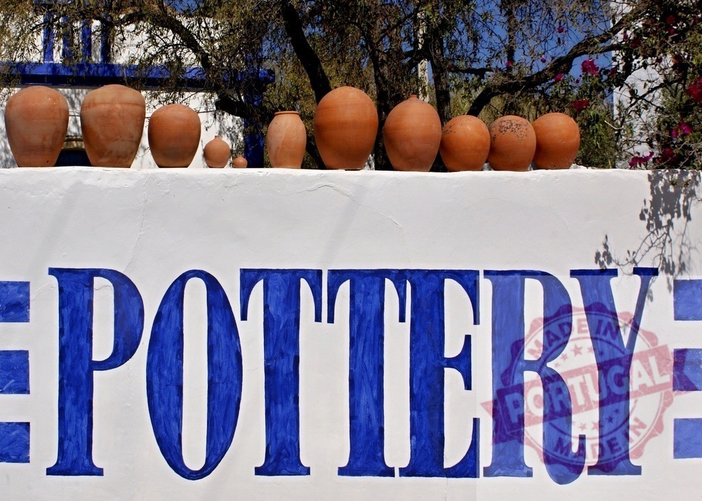 Pottery sign with terracotta pots displaying craft | Terracotta pots line a wall above a blue Pottery sign, representing traditional craftsmanship - Realisiert mit Pictrs.com