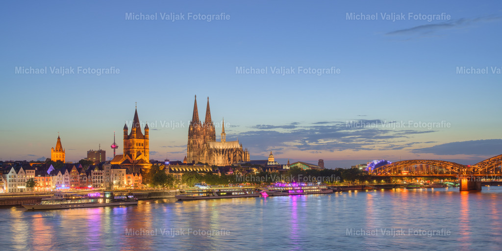 Die Skyline von Köln am Abend | Die Skyline von Köln, mit ihren beleuchteten Konturen gegen den Abendhimmel, ist ein atemberaubender Anblick. Die Silhouette des Kölner Doms, der sich majestätisch über die Stadt erhebt, wird von den Lichtern der Stadt und der Reflexion des Rheins unterstrichen. Dieses Panorama ist nicht nur ein Symbol für die Stadt Köln, sondern auch ein Zeugnis der harmonischen Verbindung von Geschichte und Moderne. Besucher und Einheimische gleichermaßen schätzen diese Aussicht, die die lebendige Atmosphäre und die Schönheit Kölns widerspiegelt. - Realisiert mit Pictrs.com